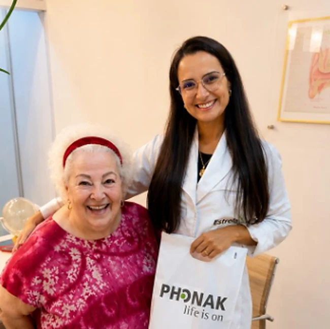 Profissional da Estrela sorrindo ao lado de uma paciente que segura uma sacola da Phonak